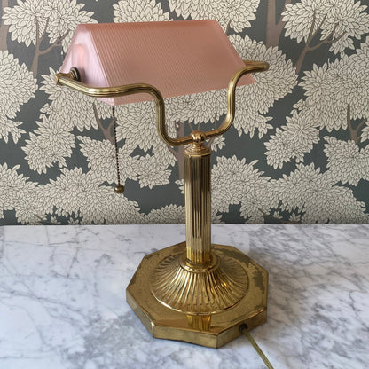 Vintage brass bankers desk lamp with ribbed pink glass shade on a marble surface with floral wallpaper background